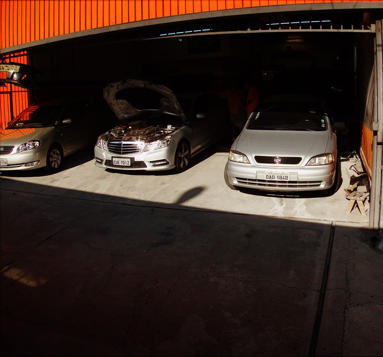 Cars being serviced in a garage, one with its hood open
